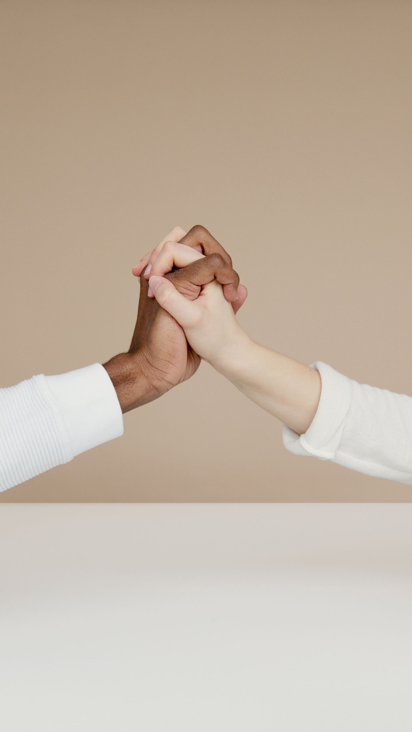 Close-up of two diverse hands gripping in a gesture of unity on a neutral background.