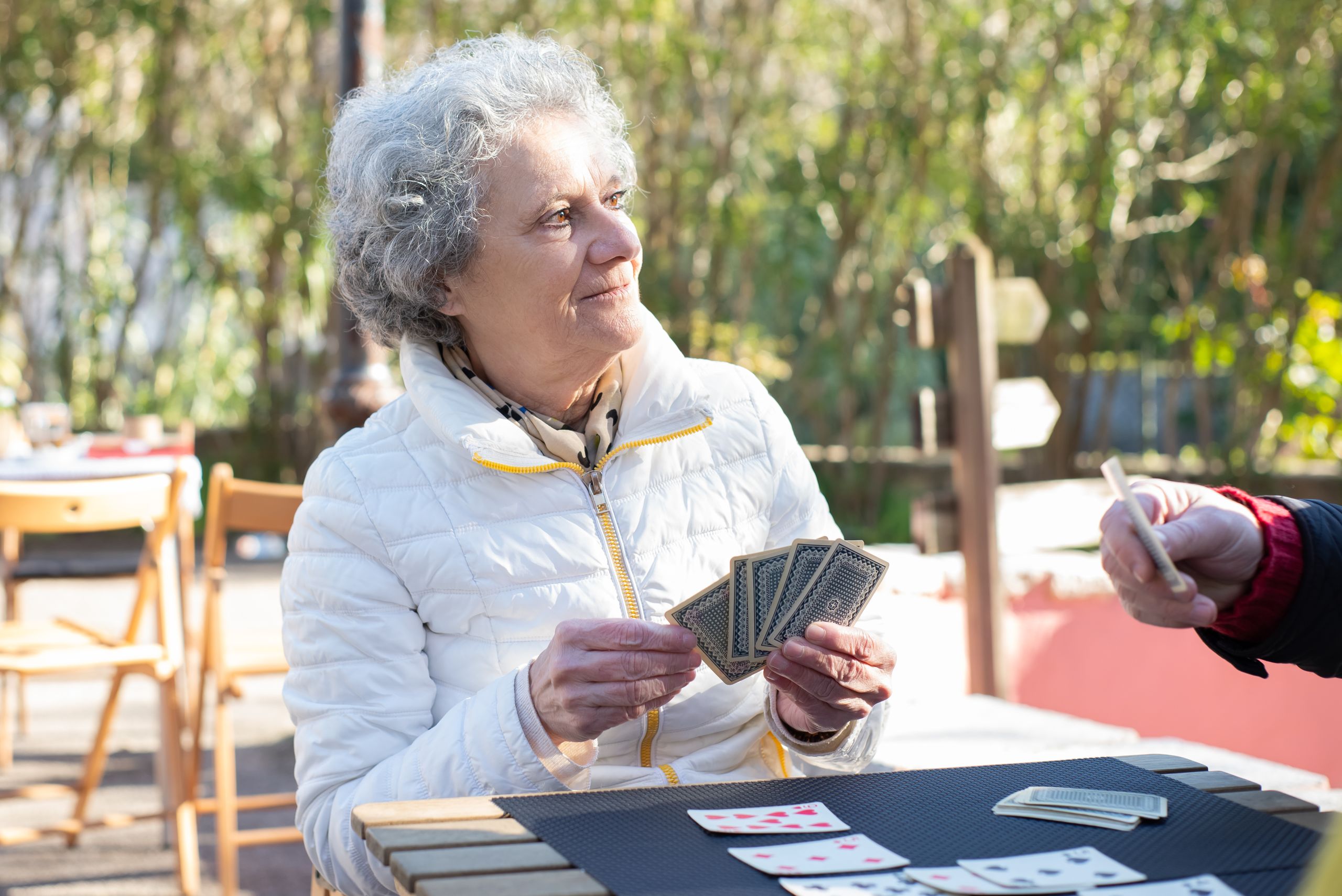 Senior woman playing cards outdoors, enjoying leisure time on a sunny day.