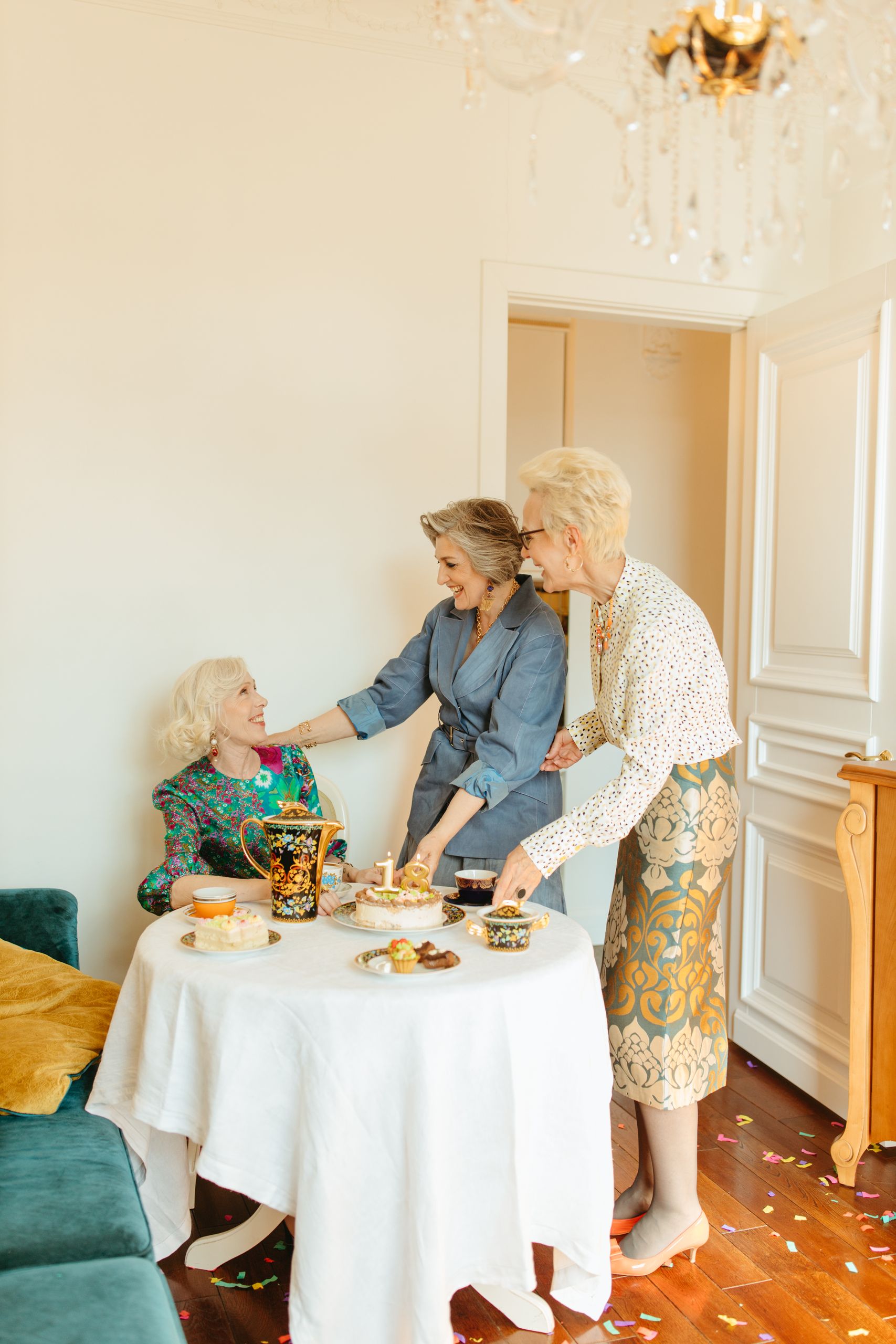 Three senior women enjoy a heartfelt indoor celebration with desserts and drinks.